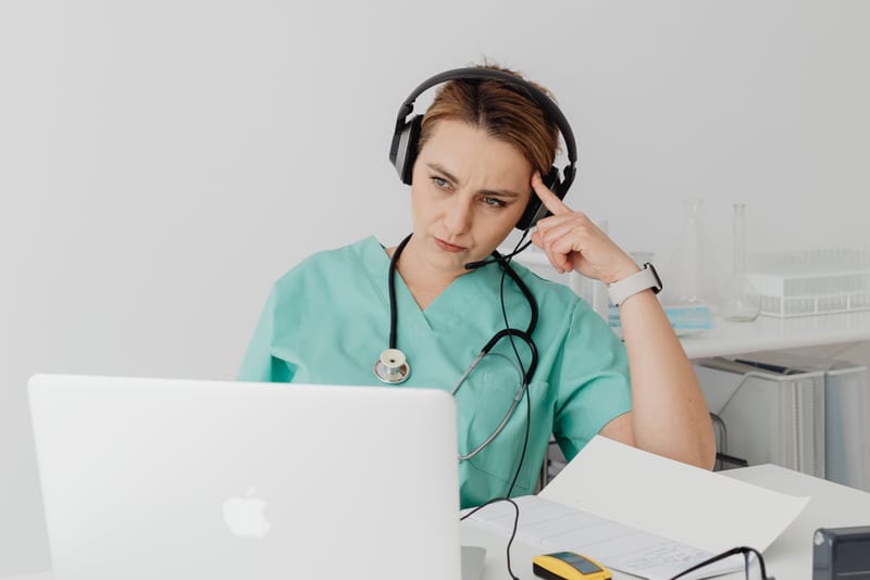 Nurse in scrubs pausing to work out the meaning behind an unfamiliar word during an OET Listening practice extract, the contextual format in action.