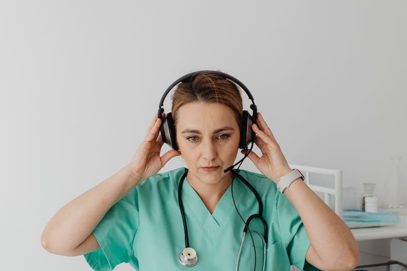 Healthcare professional in scrubs adjusting her headphones before an OET Listening Part A practice test, where the audio plays once only.