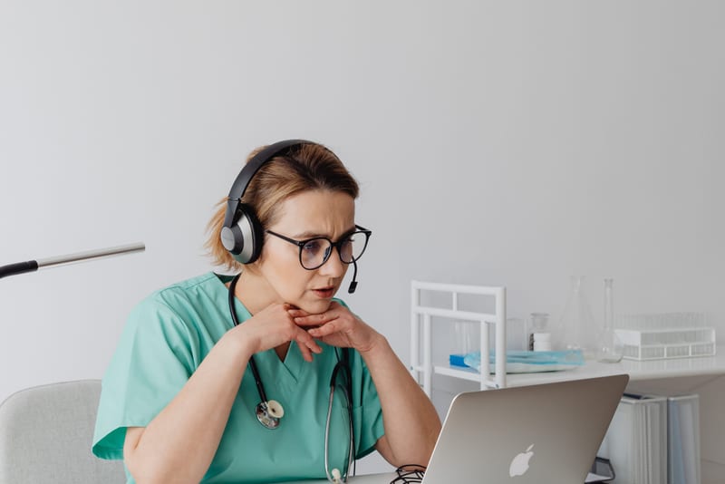 Healthcare professional in scrubs listening closely through a headset, working out which OET Listening Part B question type the extract belongs to.