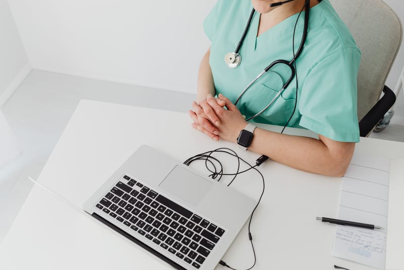 Overhead view of a healthcare professional at a laptop with a headset and a written practice log, the weekly OET Listening preparation system in use.